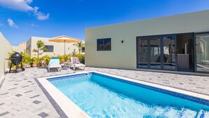 A swimming pool with lounge chairs and a grill, surrounded by a paved patio and a building with large windows.