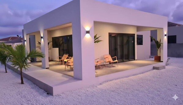 A modern building with a covered patio area, outdoor seating, and a gravel ground.