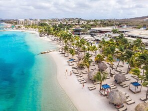 A beach resort with sun loungers, palm trees, and a view of the ocean.