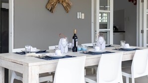 A dining table set with white plates, glasses, and cutlery, with a bottle of wine and a decorative wall piece.