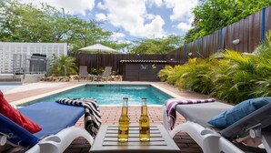 A backyard with a swimming pool, lounge chairs, and two bottles of beer on a table.
