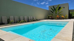 Una piscina rectangular con agua azul cristalina, rodeada por una terraza de baldosas de color claro.