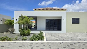 Una casa moderna de dos pisos con techo de tejas, un patio con plantas y un camino de entrada pavimentado.