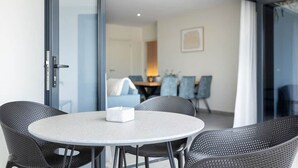 Una habitación moderna con una mesa redonda y cuatro sillas, una puerta de cristal corredera que da a un comedor y un cuadro enmarcado en la pared.