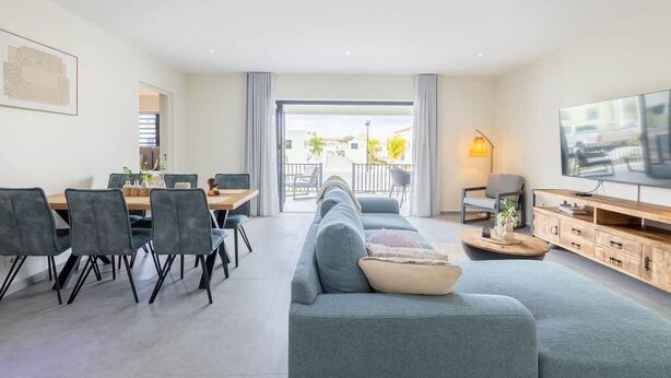 Una sala de estar moderna con un sofá, una mesa de comedor, sillas y un televisor.