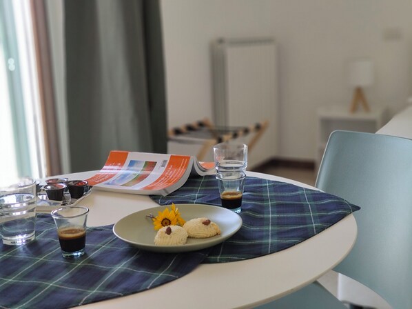 A table with a plaid placemat, a plate with cookies and a flower, a glass of water, a glass of coffee, and a magazine. - SEA DREAM PALACE 3 (Trani)