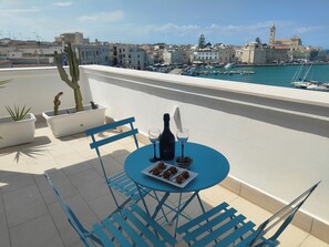 A terrace with a table set for two, featuring a bottle and glasses, and a plate of cookies.