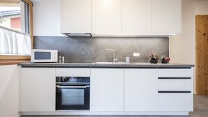 A modern kitchen with white cabinets, a built-in oven, a microwave, and a window with a view of the outside. - 305B Apartments No 10 (Ponte Gardena)