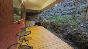 A wooden deck with a brick wall and a stone wall, two wicker chairs, and a small table.