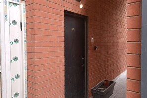 Un mur de briques avec une porte noire, un chambranle de porte blanc et une petite poubelle.