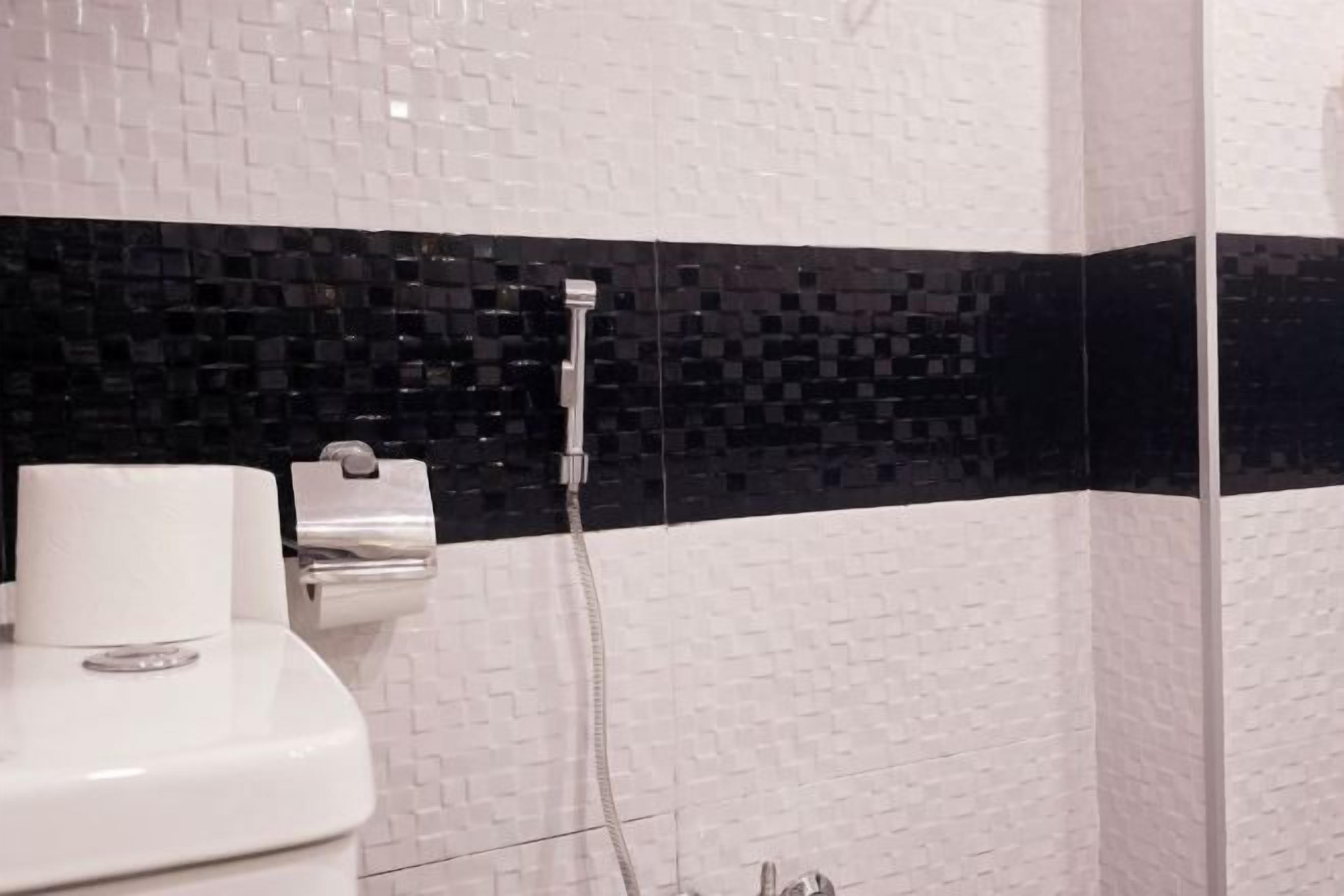 A bathroom with a toilet, a paper towel dispenser, and a shower head.