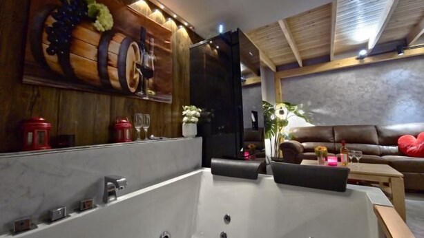 A modern bathroom with a large bathtub, wooden wall decor, and a seating area with a couch and table.