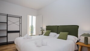 A neatly made bed with white linens and green pillows, a wooden floor, a metal wardrobe, and a window with natural light. - Torre dels Bous Apartment 1-A (Hostalric)