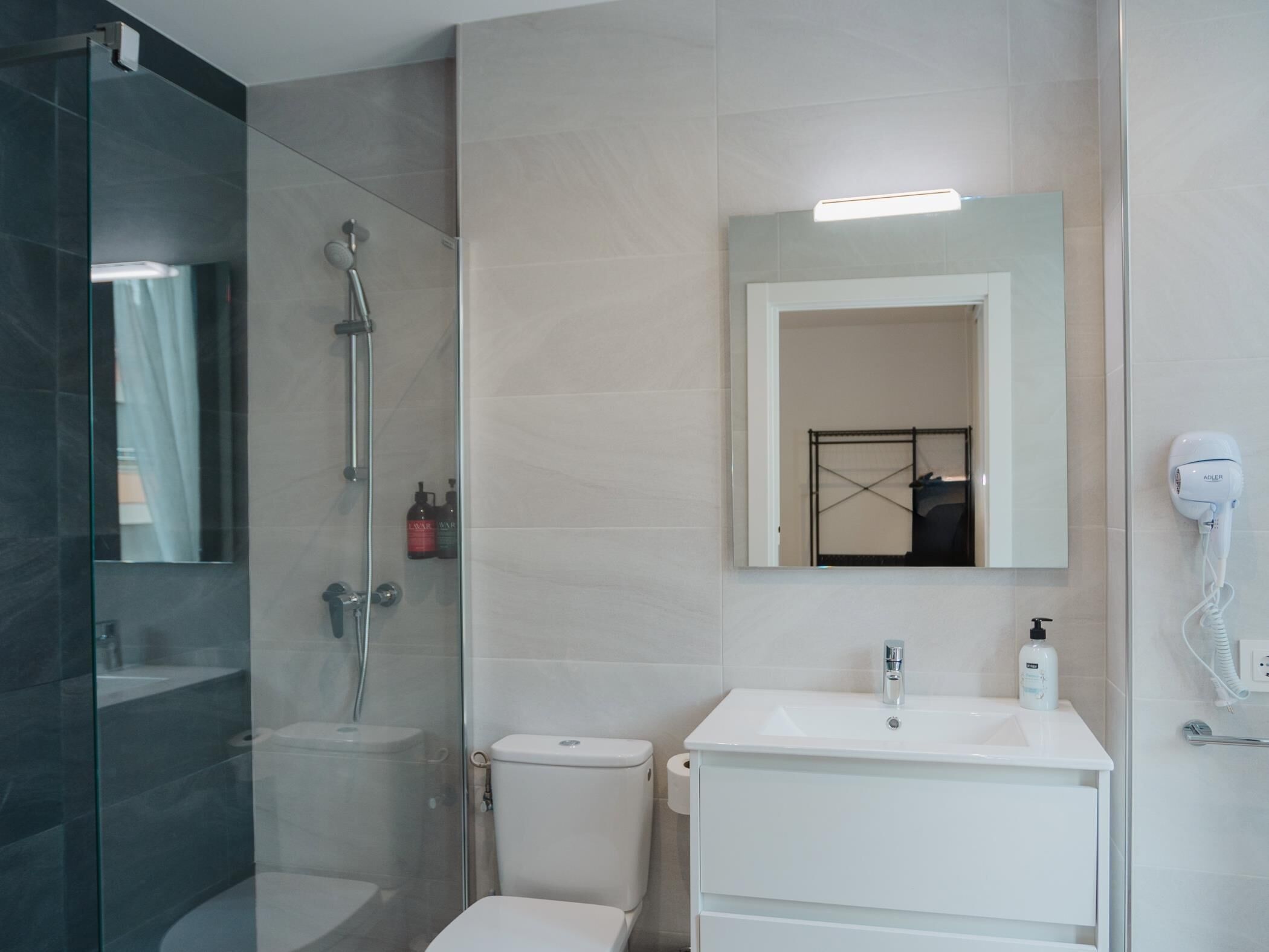 Un baño moderno con ducha de vidrio, un lavabo blanco y un espejo sobre él.