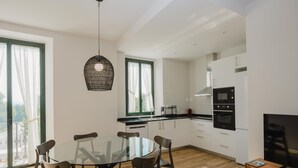 A modern kitchen with white cabinets, a black oven, and a wooden dining table with chairs. - Torre dels Bous Apartment 1-A (Hostalric)