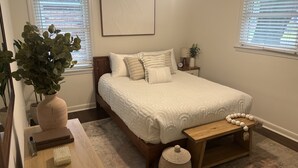 Ein ordentlich eingerichtetes Schlafzimmer mit einem Bett, Nachttischen, einer Nachttischlampe und einer großen Topfpflanze.