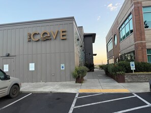 Een gebouw met het bord 'COVE' op de gevel, een parkeerplaats met aangegeven parkeerplaatsen, en een heldere lucht.