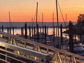 A marina with boats docked, a bridge in the foreground, and a sunset in the background.