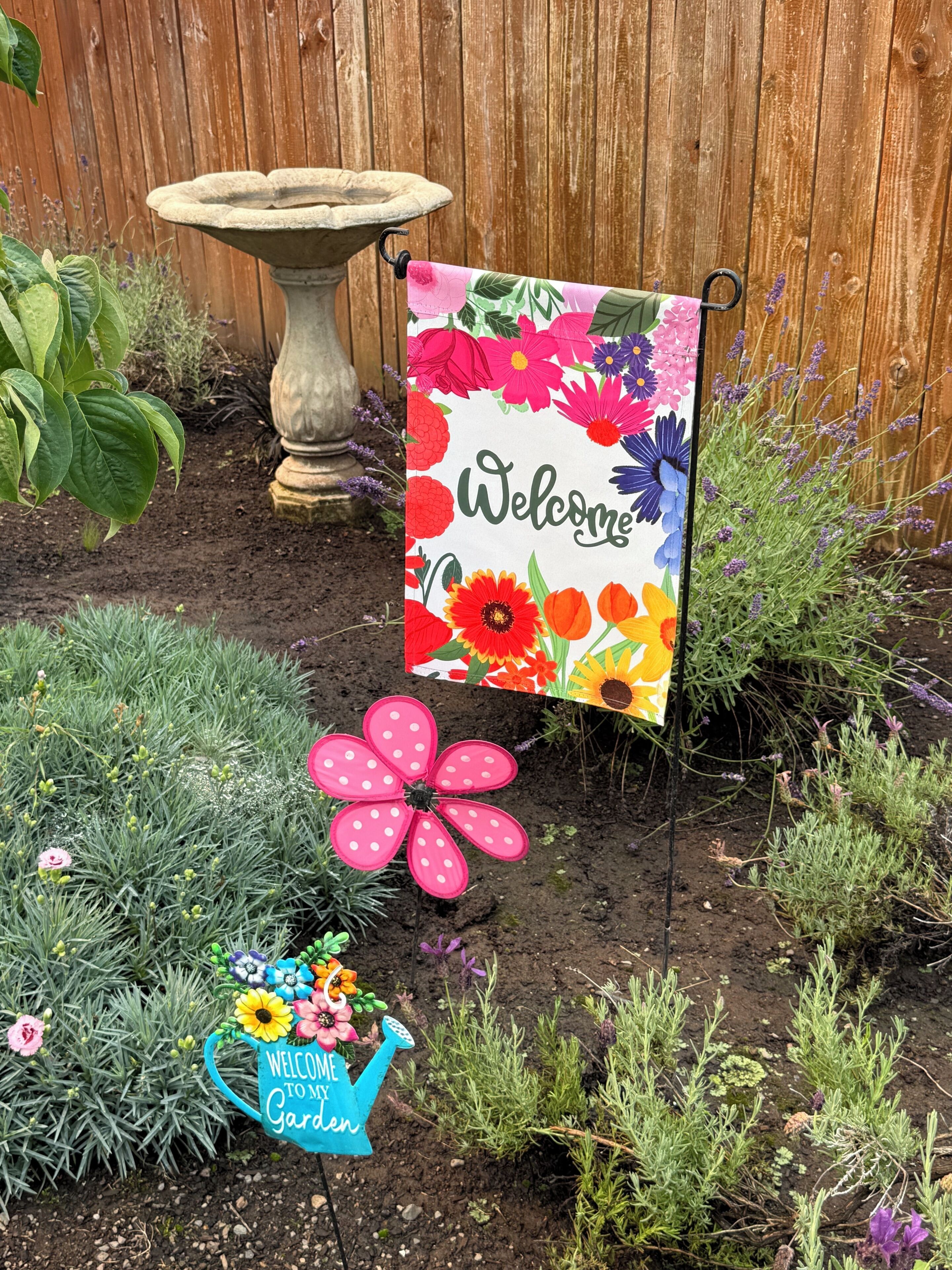 A garden with a welcome sign, a decorative flower pot, and a watering can sign.