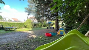 A backyard with a green slide, a red tire, and a blue umbrella.