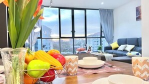 A modern living room with a dining table set for two, a sofa, and a large window offering a city view.
