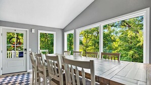 A dining area with a large table and chairs, large windows with a view of trees, and a checkered floor mat. - Greens and Gators For 20ppl (Lake Ozark)