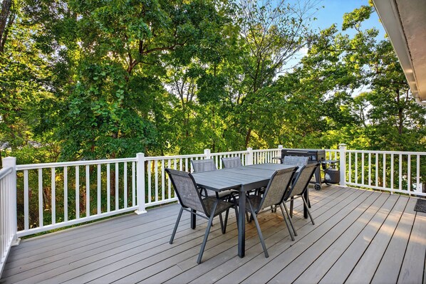 A deck with a table and chairs, surrounded by a white railing, overlooking a lush green landscape.