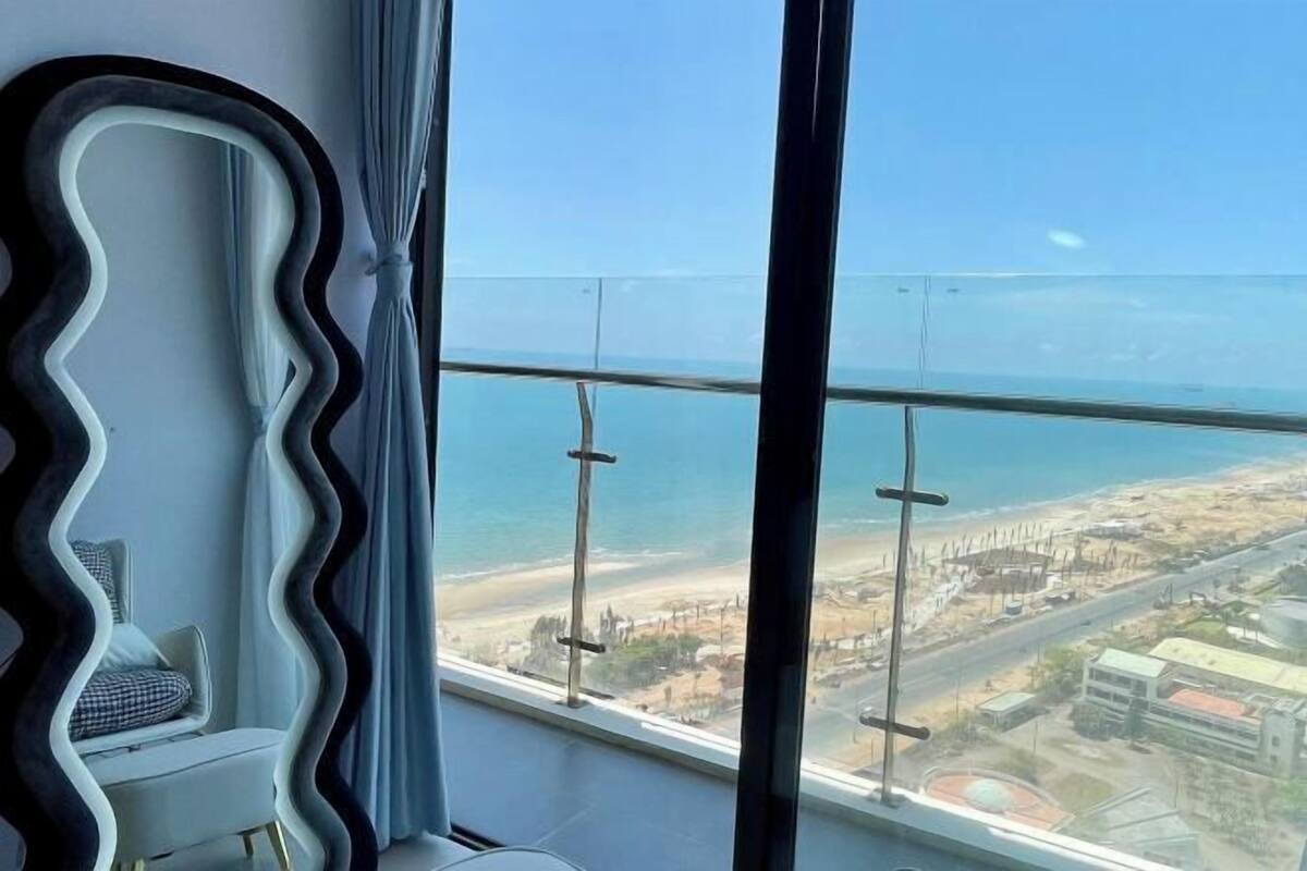 Ein Zimmer mit Blick auf den Strand, ein Sessel, ein großes Spiegel und ein Fenster mit Stadtblick.