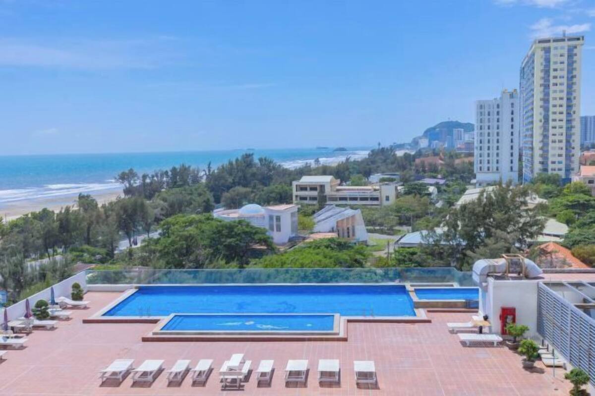 Ein Pool auf dem Dach mit Liegestühlen, Blick auf das Meer und umliegende Gebäude.