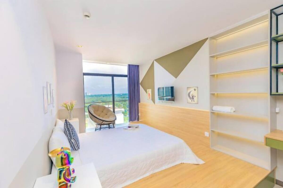 Ein modernes Hotelzimmer mit einem großen Bett, einem Sessel, einem Fernseher und Blick ins Freie.