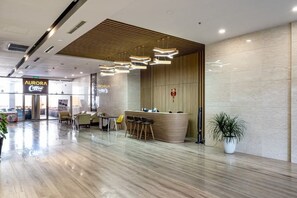 A modern hotel lobby with a reception desk, seating area, and a coffee shop in the background. - Nha Cua Mang - CSJ Tower Bai Sau Vung Tau (Vung Tau)