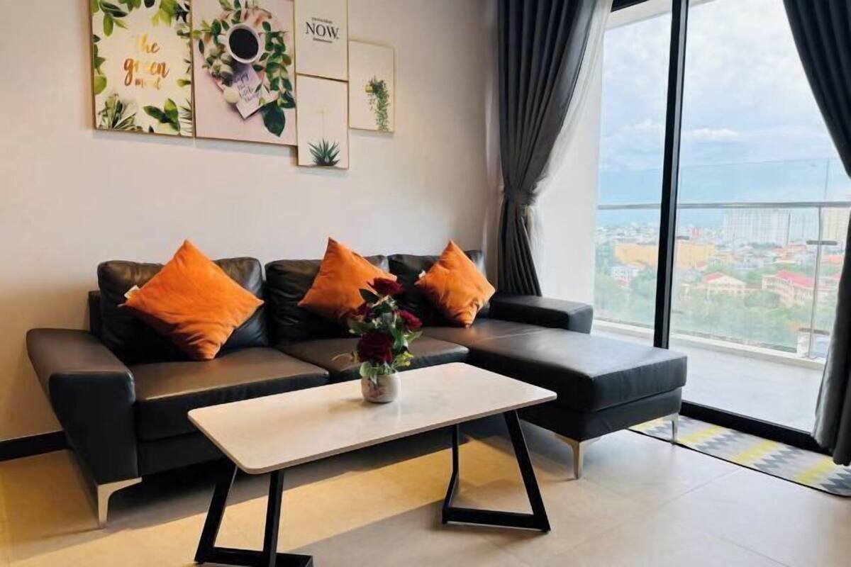 Ein modernes Wohnzimmer mit einer Couch, einem Couchtisch und Blick auf eine Stadtlandschaft durch große Fenster.