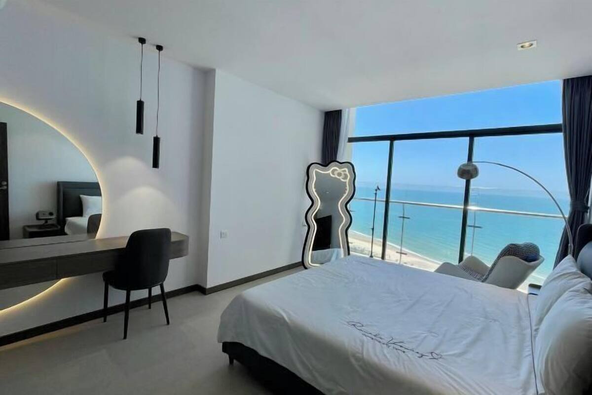 Ein modernes Hotelzimmer mit einem großen Bett, einem Schreibtisch, einem Sessel und Meerblick.