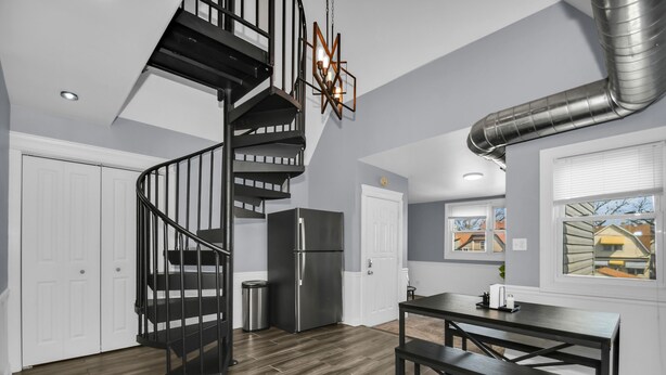 A modern kitchen with a black spiral staircase, stainless steel refrigerator, and a dining area with a table and benches.