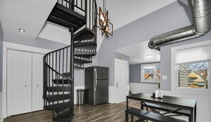 Une cuisine moderne avec un escalier en colimaçon noir, un réfrigérateur en acier inoxydable et un coin repas comprenant une table et des bancs.