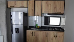 Una cucina compatta con mobili in legno, un frigorifero in acciaio inox, un piano cottura a gas e una finestra sopra il lavello.
