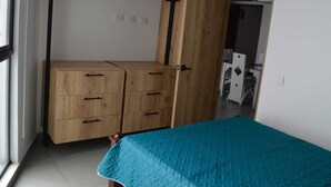 Una camera da letto con un letto, un armadio in legno con cassetti e una porta che dà su un'altra stanza.