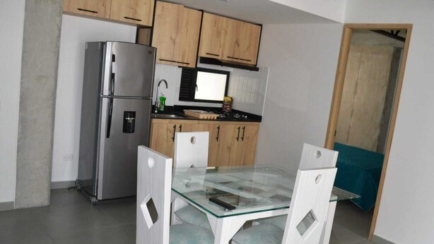 Una cucina compatta con mobili in legno, un frigorifero in acciaio inossidabile e un tavolo da pranzo in vetro con sedie.