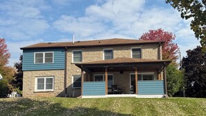 A two-story house with a stone facade and blue siding, featuring a covered patio area.