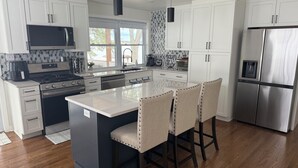 A modern kitchen with white cabinets, stainless steel appliances, a central island with bar stools, and a large window providing natural light.