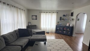 A living room with a sectional sofa, ottoman, and a coffee table. There is a cabinet with decorative items and a door leading to another room.