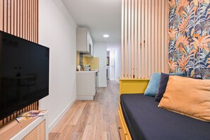 A modern room with a flat-screen TV, a sofa with cushions, a kitchen area, and a patterned wall. - ✨ Stylish & Bright Studio – Historic Center of Aix-en-Provence (Aix-En-Provence)