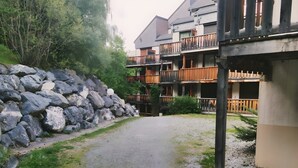 Un sendero de grava que conduce a un edificio con varios balcones, rodeado de vegetación y un muro de piedra.
