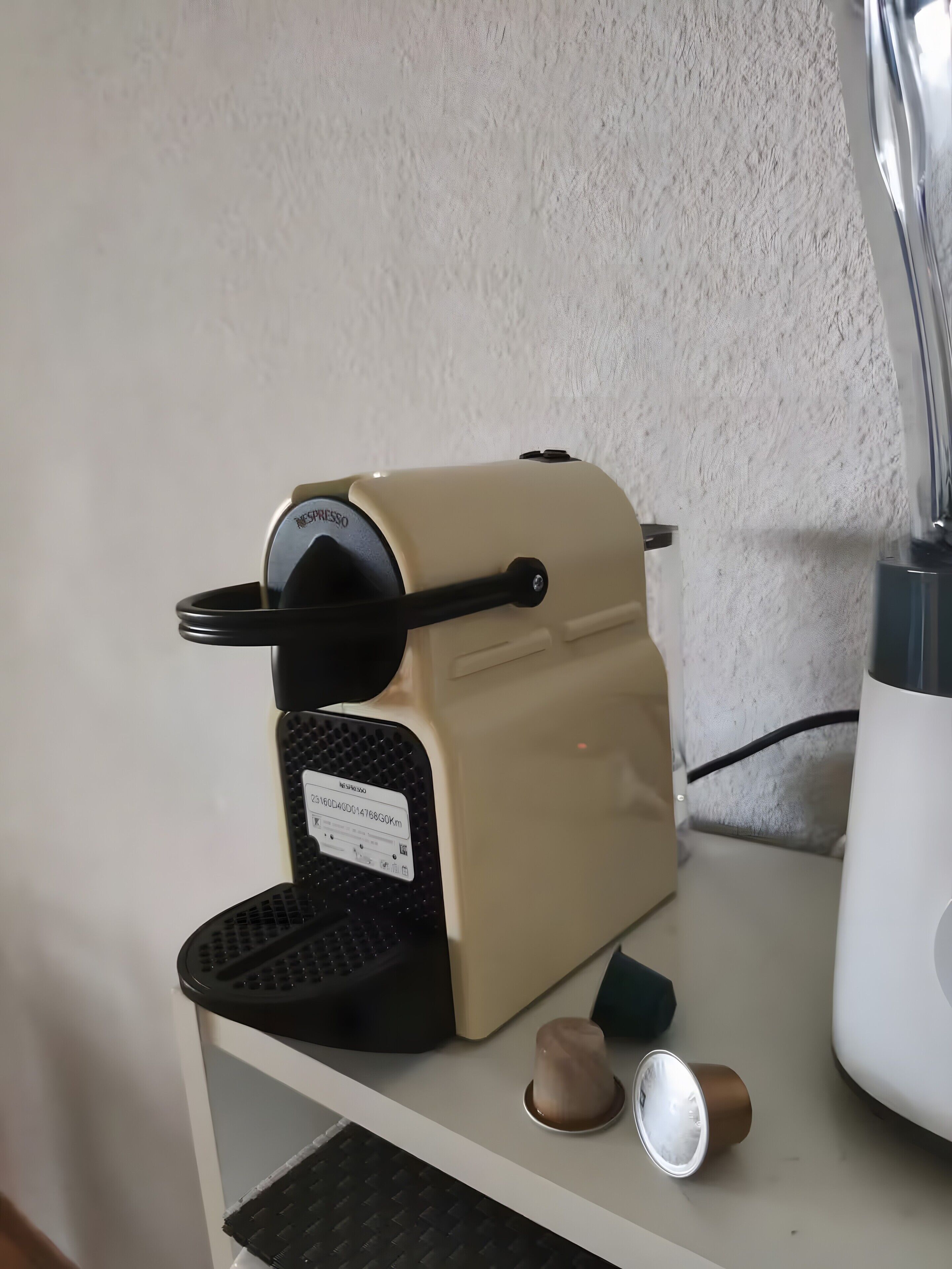 Une machine à café posée sur un plan de travail de cuisine, avec un mur blanc à texture visible en arrière-plan.