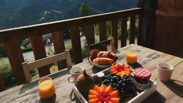Una mesa de madera con alimentos para el desayuno y una vista panorámica de la montaña.