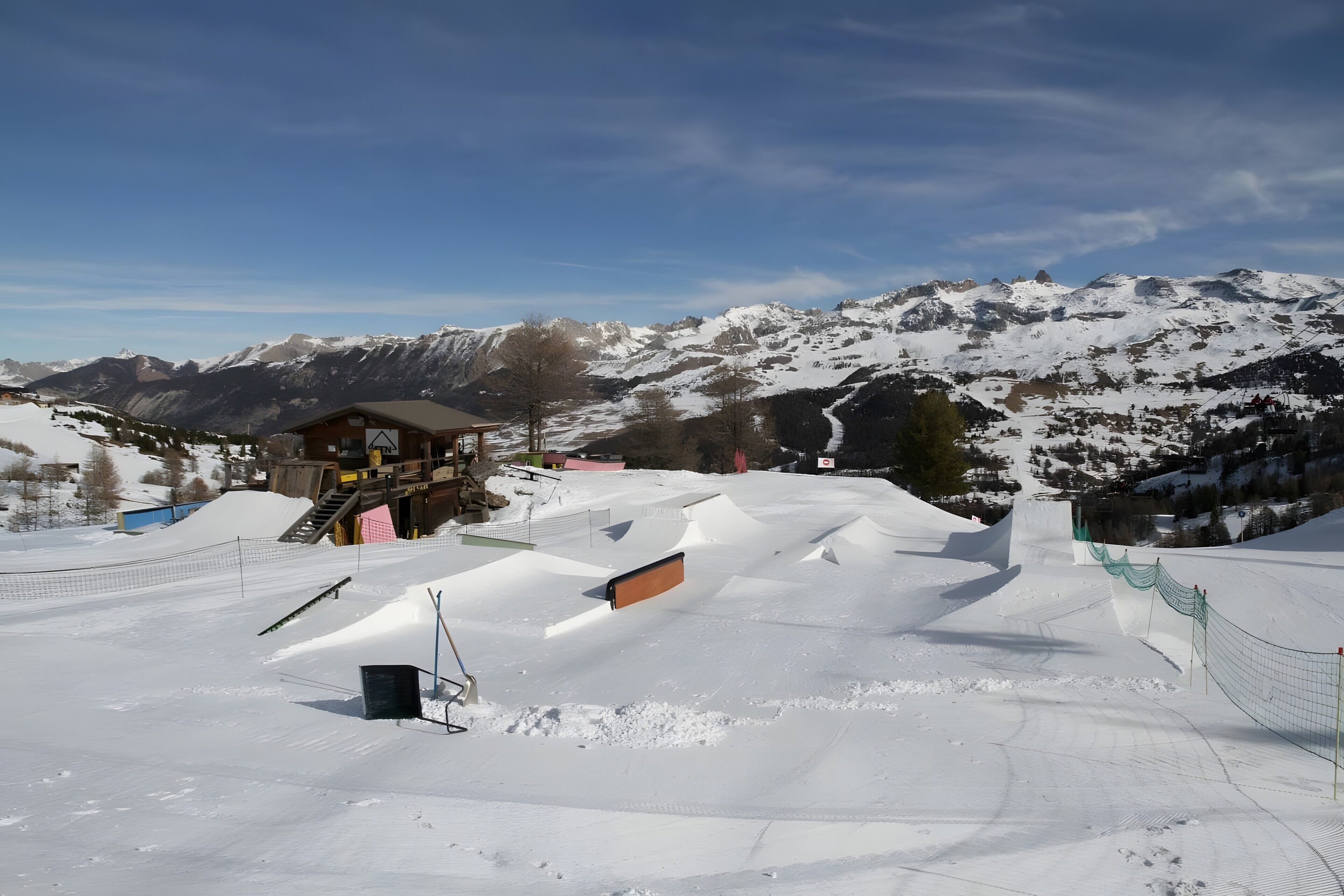 A snow-covered ski slope with a wooden cabin and a mountain backdrop.