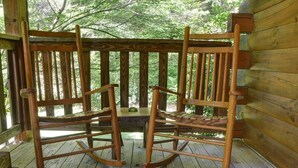 Een houten schommelstoel op een terras met houten balustrade en een houten wand.