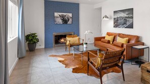 A modern living room with a blue brick accent wall, a fireplace, leather furniture, and two large wall art pieces. - Private Pool and Spa in Palm Springs with Mid Century Style and Mountain Views (Palm Springs)
