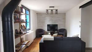 Ein modernes Wohnzimmer mit einer Couch, zwei Sesseln, einem Fernseher und einem Bücherregal.