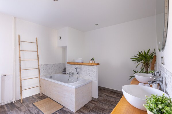 Un baño moderno con bañera, lavamanos, una escalera de madera y un estante con artículos de aseo.